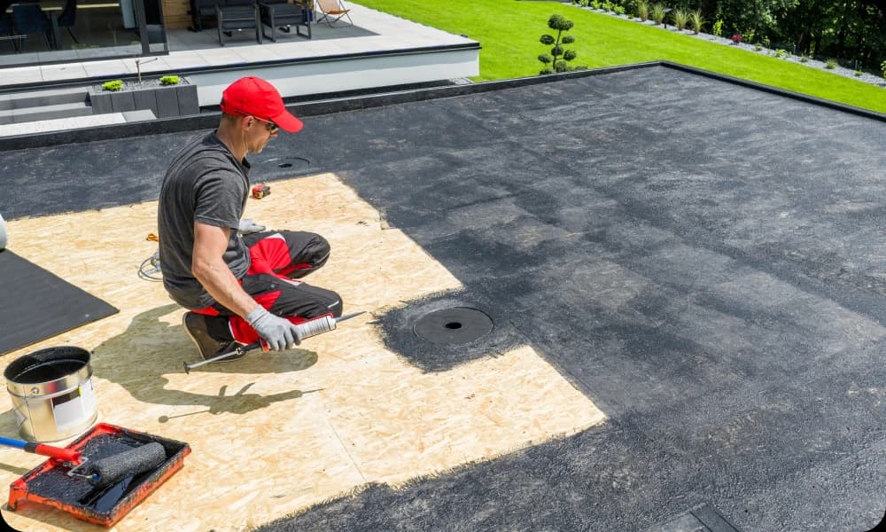 a roofer dressed in protective clothing painting waterproof paint onto the flat roof deck