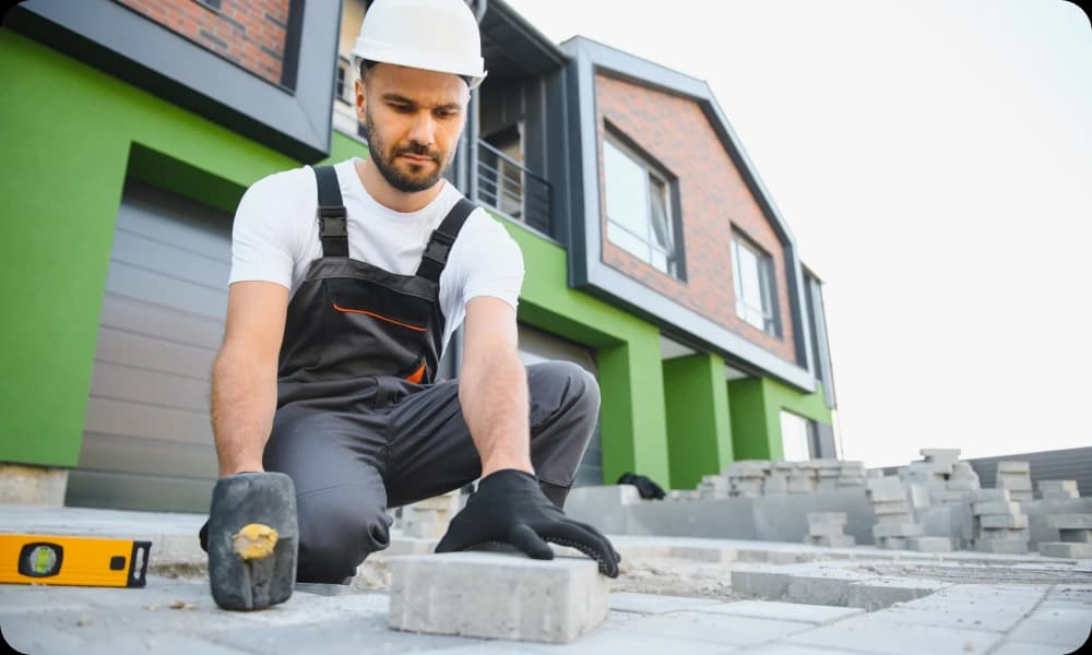 expert laying pavers for patio, gloves on and a rubber mallet in hand