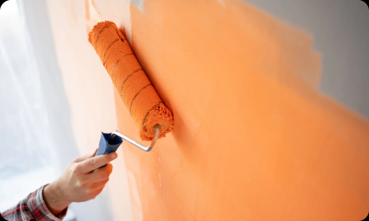 Paint roller, rolling on bright orange paint on the wall