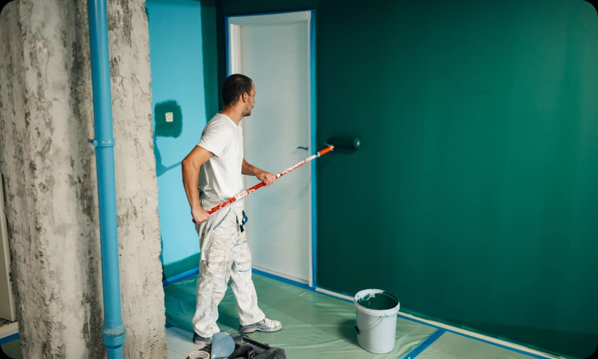  professional painter using a long roller to paint the wall a dark green