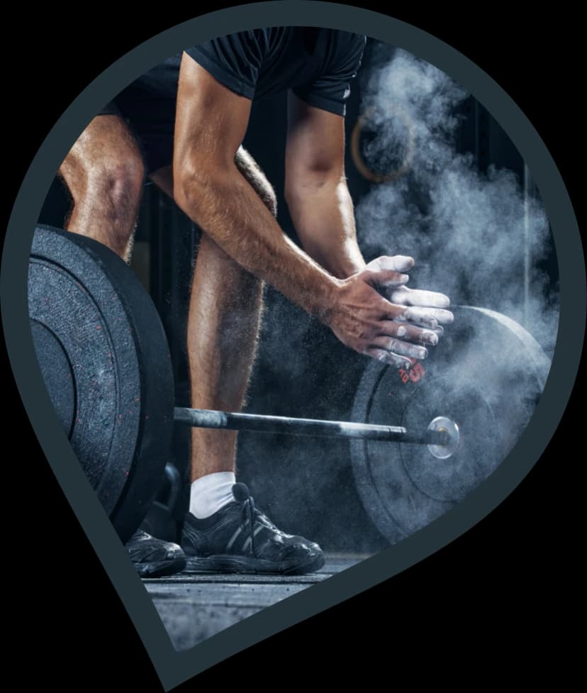 WEIGHT LIFTER CHALKING HIS HAND, KNEELING DOWN TO COMPLETE A BARBELL DEADLIFT.