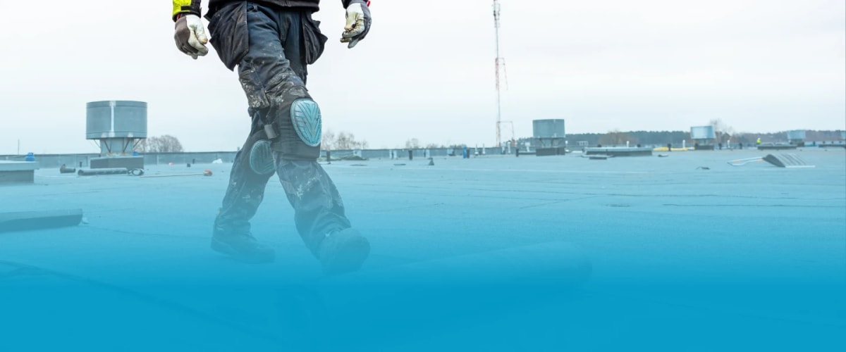 a roofer wearing protective clothing unrolling roofing material on a flat roof