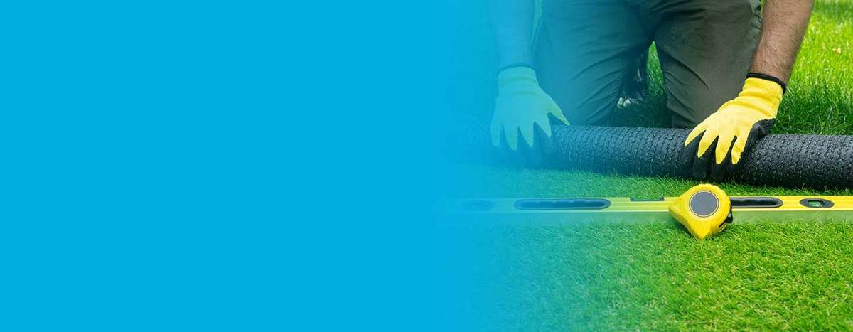 Artificial grass installer landscaping a yard with artificial grass, measuring tap on grass.