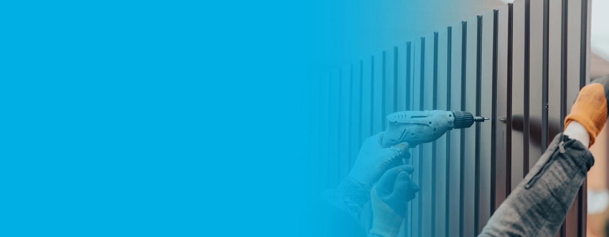 Worker drilling metal fence panel