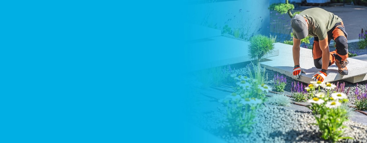 A Landscaper carefully laying a large concrete slab amongst a garden of flowers and grey pebble dash