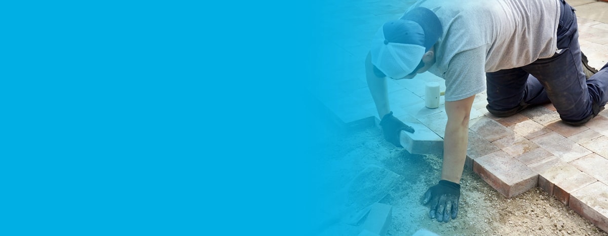 Expert patio installer with gloves on, laying paver bricks on large patio